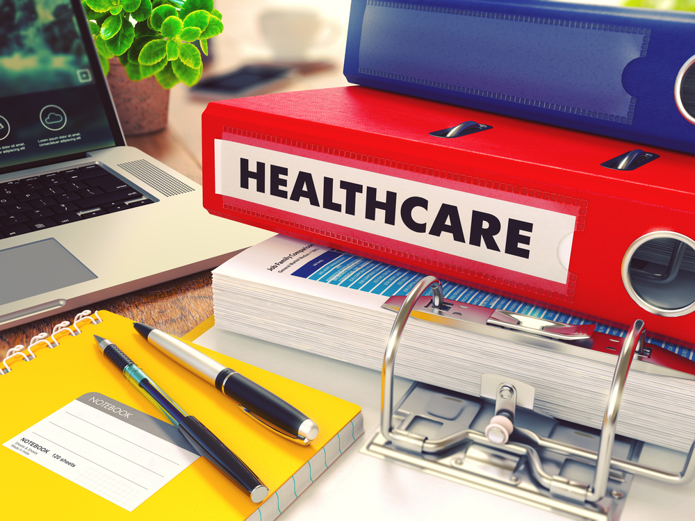 Healthcare - Red Office Folder on Background of Working Table with Stationery, Laptop and Reports. Business Concept on Blurred Background. Toned Image.